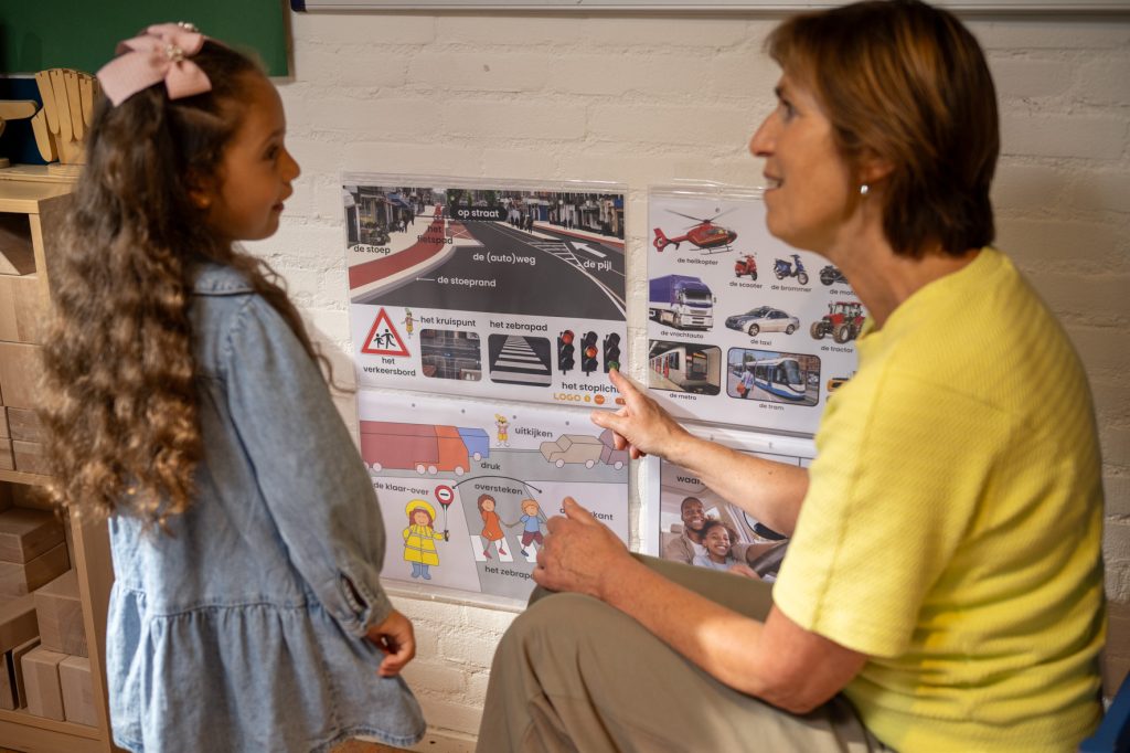 Leerkracht en kind staan voor een woordmuur met LOGO woordwebben
